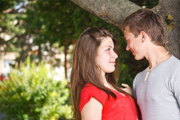 Girl and guy smiling at each other with a tree in the background