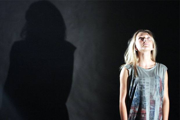 Girl looking up, standing against black backround with her shadow behind her