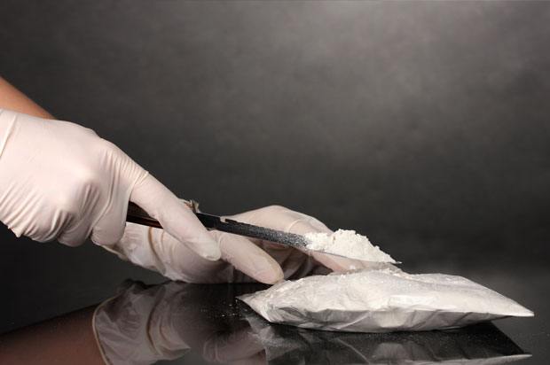 Hands with gloves using a knife to open a packet of cocaine