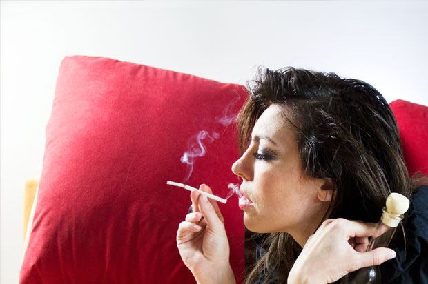 Girl smoking on bed next to a pillow