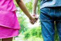 Couple walks through wooded area holding hands.