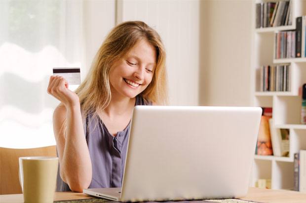 Girl smiling looking at her laptop holding a debit card