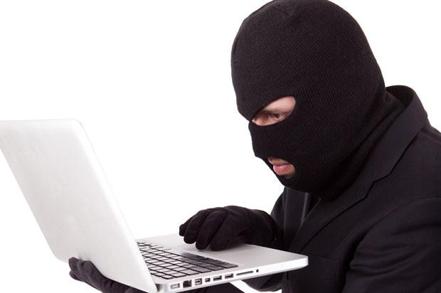 Man on a laptop wearing a balaclava.