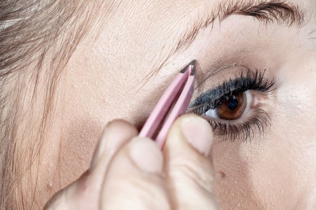 Close up of girl plucking her eyebrows with tweezers