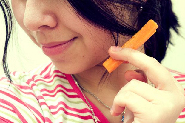 Girl holding a carrot between her fingers like she's smoking