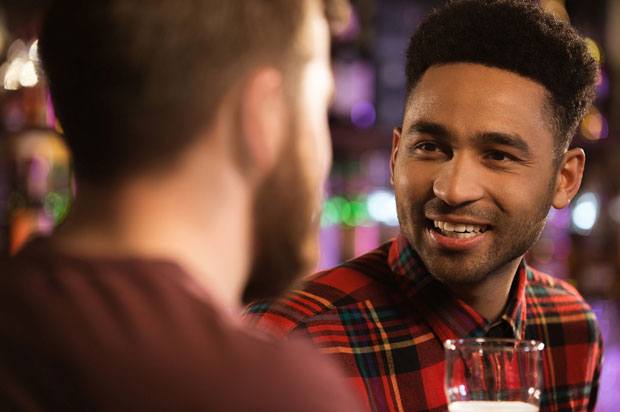 men stand at a bar having a conversation.