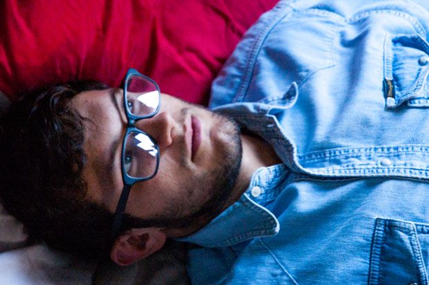 Guy with glasses and a denim shirt lying on his bed