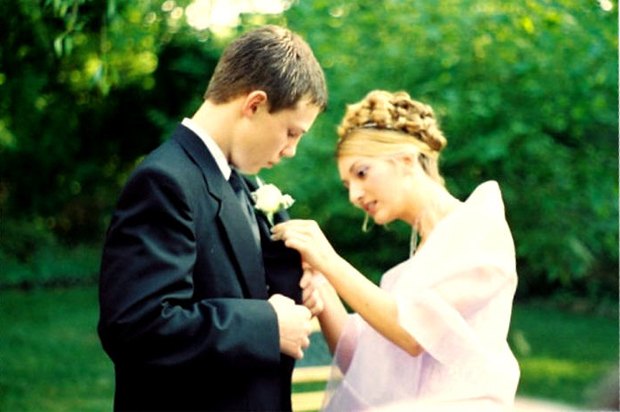 girl in prom dress pinning a corsage onto a boy's tux