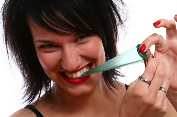 Girl pulling at a condom with her teeth.