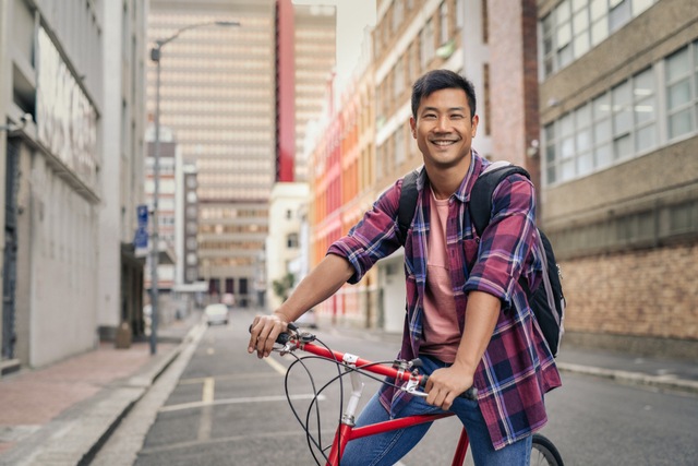 A young man with a bike smiling at the camera in an alleyway
