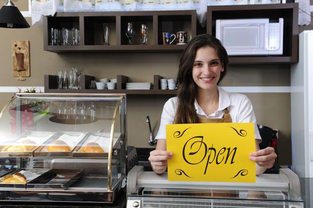 Girl in shop holding the open sign.