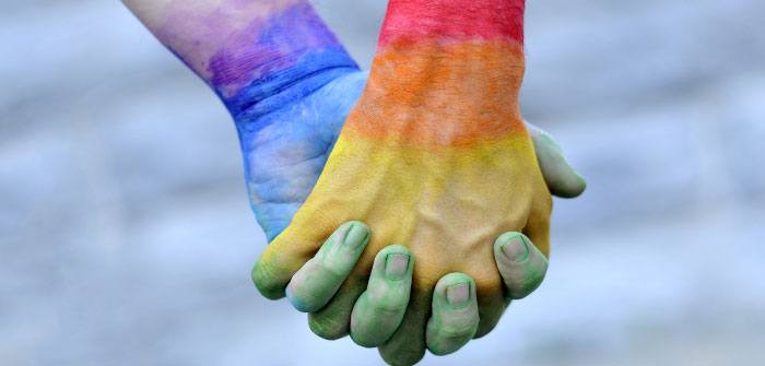 two hands intertwined covered in gay pride coloured paint