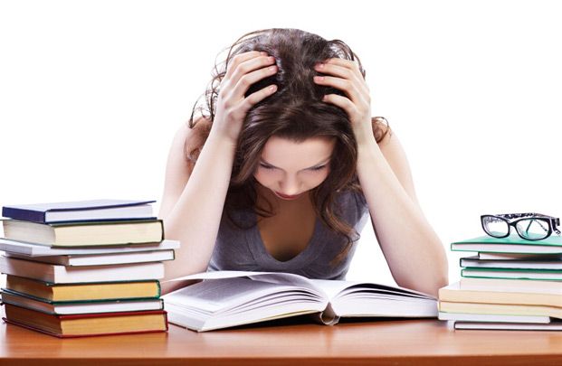 girl with head in hands looking stressed over books