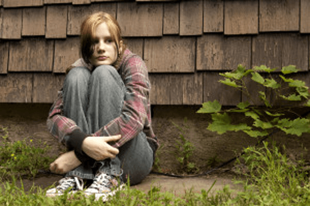 Young girl sits on the ground with her back to a wall looking afraid