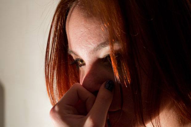 A girl with red hair looks into the distance. Half of her face is in shadows.