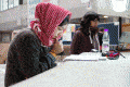 Girl in a red headwrap bites her thumb and looks down at her desk.
