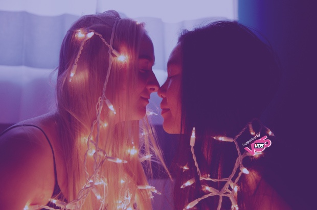 Two girls smiling at eachother with pixie lights over their heads in the dark