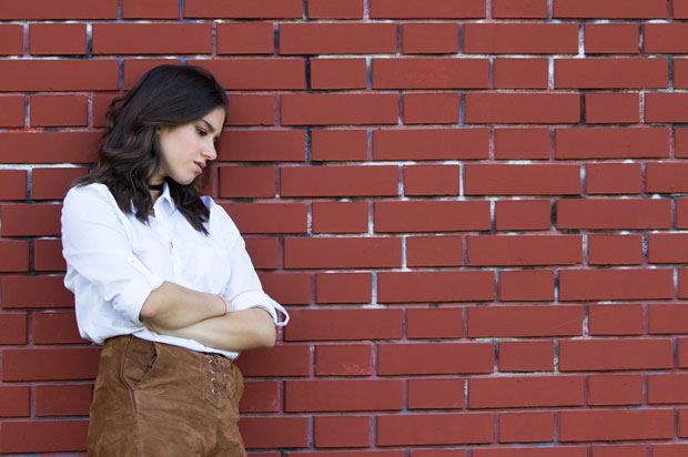 woman stand against a brick wall looking upset.