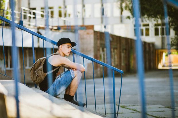 person sits on steps outside a large building. There are railings in front of the camera.