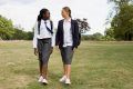 Two school girls walk across an open field talking to each other.